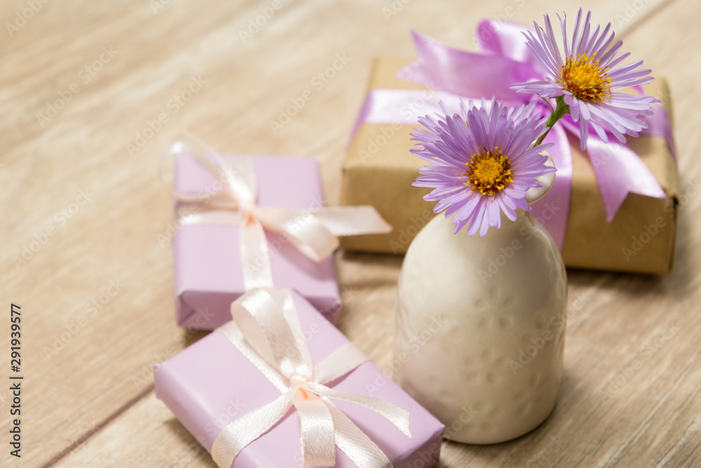 Purple spring flowers in a white vase on a wooden table. Gift box wrapped in craft paper with ribbon Purple spring flowers in a white vase on a wooden table. Gift box wrapped in craft paper with ribbon