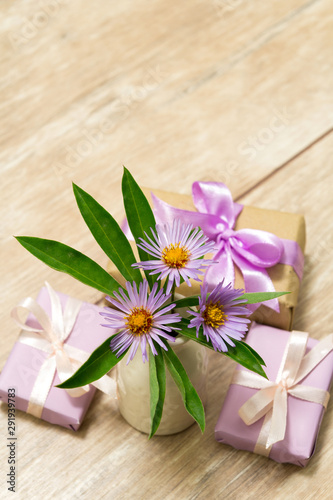 Fototapeta Naklejka Na Ścianę i Meble -  Purple spring flowers in a white vase on a wooden table. Gift box wrapped in craft paper with ribbon