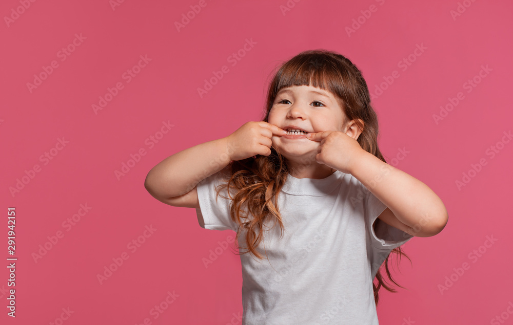 Close-up portrait of a little brunette girl dressed in a white t-shirt posing against a pink studio background. Sincere emotions concept. Close-up portrait of a little brunette girl dressed in a white t-shirt posing against a pink studio background. Sincere emotions concept.