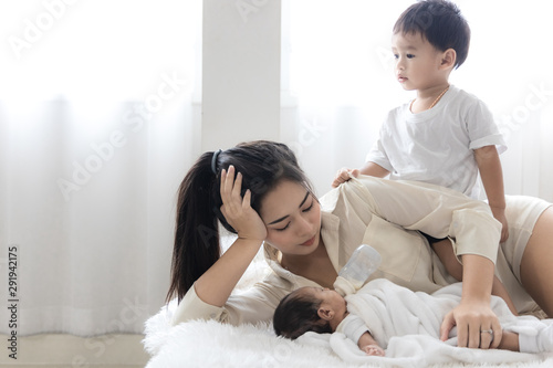 Young Asian mother hugging a cute newborn baby and feeding milk form bottle in with the son white bedroom. Duty of the wife to raise children. Mother and child concept