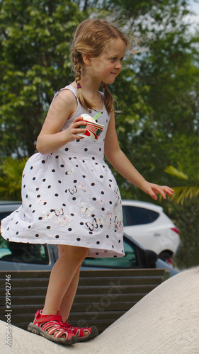 Little blonde girl eating ice cream with a spoon from a paper cup