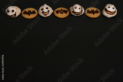 Homemade cakes for Halloween. Scary smiley ghosts meringue and cookies with bats on black background.