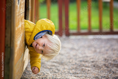Blonde little toddler child in yellow jacket, playing on the playground