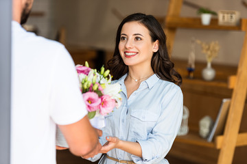 cropped view of delivery man giving flowers to happy woman