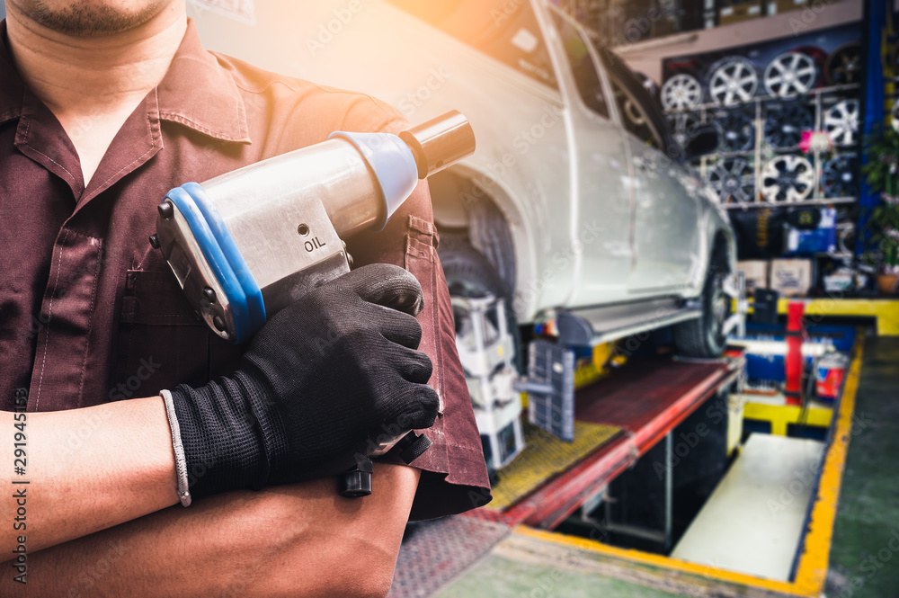 The abstract image of the technician holds an air wrench and blurred wheel alignment machine image is the backdrop. the concept of automotive, repairing, mechanical, vehicle and technology.	