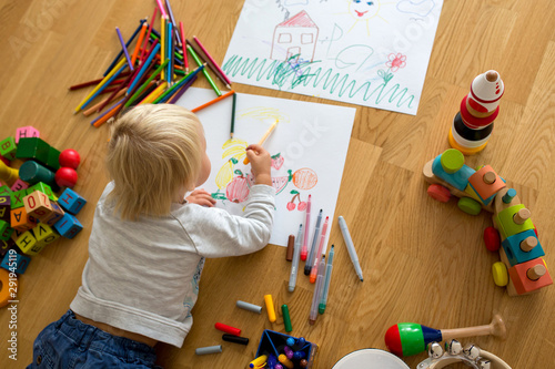 Little blonde toddler boy  drawing with pastels and coloring pens  playing with wooden toys