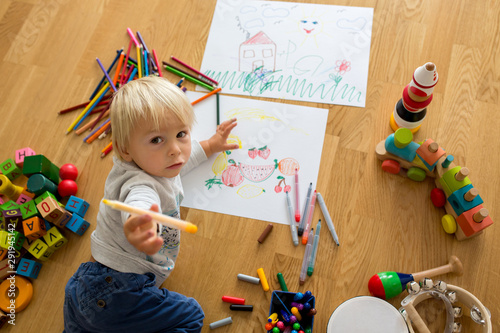 Little blonde toddler boy  drawing with pastels and coloring pens  playing with wooden toys