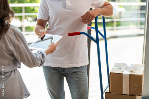 cropped view of delivery man standing near delivery cart with boxes and woman with digital tablet