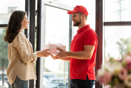 selective focus of handsome delivery man in cap giving pink present to happy woman