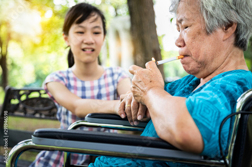 Asian child girl ask a smoker to stop smoke is dangerous to health and those around, trying to stop,warning or prohibiting senior grandmother in wheelchair,elderly holding a cigarette smoking in park