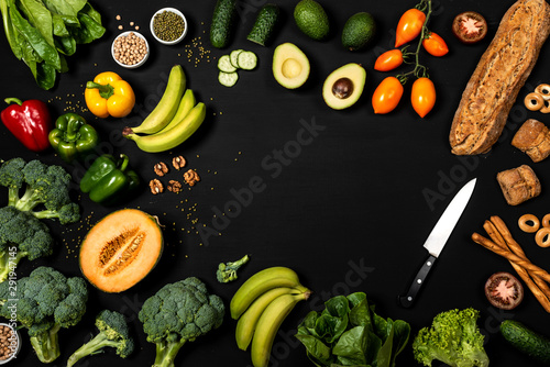 Fototapeta Naklejka Na Ścianę i Meble -  Frame of different vegetables and bread products on a black background with place for text. Balanced diet or cooking concept. Healthy vegan food. Top view.