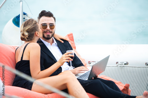 Two luxury business people sit on bean bag and working with laptop on a sailing boat. Concept business travel