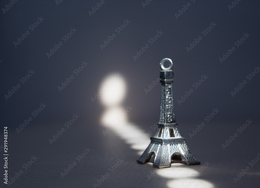 Close up shot of a miniature model of the Eiffel Tower on a dark background with sun beam. 