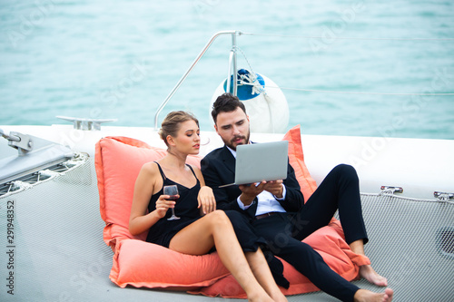 Two luxury business people sit on bean bag and working with laptop on a sailing boat. Concept business travel
