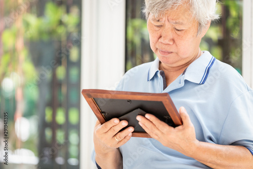 Depressed asian senior woman waiting for the family to visit her with holding a picture frame and watching old photographs ,sad elderly moaning over an old photograph,missing lover at nursing home