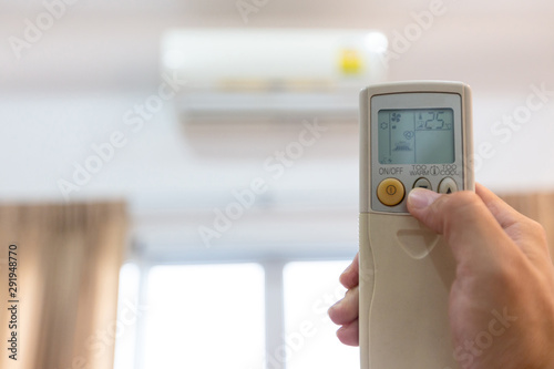 Woman holding a remote control with air conditioner,controlling the temperature,adjust air conditioner to 25 degrees celsius,energy saving campaign,save electricity bill and environment,global warming