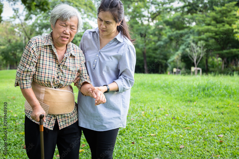 Asian senior mother backache use back support belt for protect her back pain,muscle  injury,middle-aged daughter or care assistant help,support elderly woman  feel sudden back pain while walking at park Stock Photo