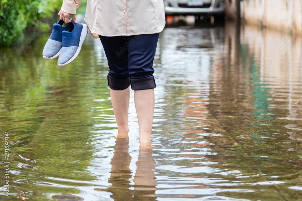 Φωτογραφία Woman walking on flooding road with holding shoes after the heavy rains,cause of