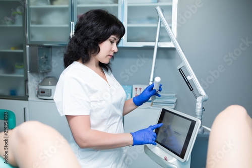 Caucasian female gynecologist with dark hair  in a white coat and blue sterile gloves makes a vaginal ultrasound to the patient