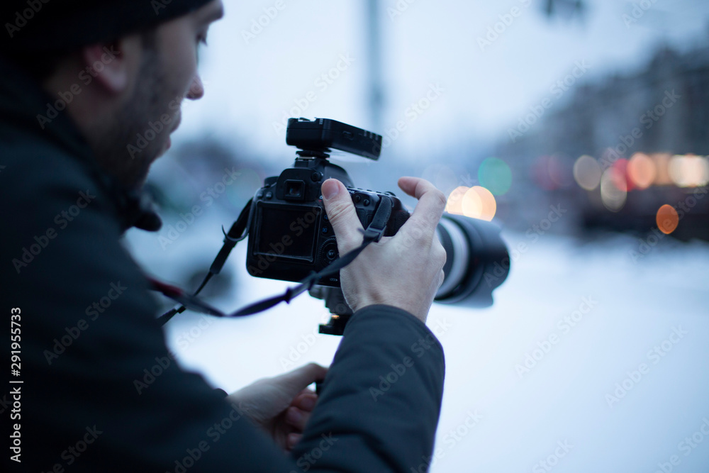 photo of a man from behind with a camera in his hands photographing winter city streets, a photographer against the background of an evening city. selective focus, noise effect photo of a man from behind with a camera in his hands photographing winter city streets, a photographer against the background of an evening city. selective focus, noise effect
