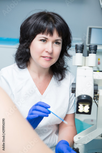 Canvas-taulu woman in a white coat and blue gloves doctor gynecologist examines a patient on