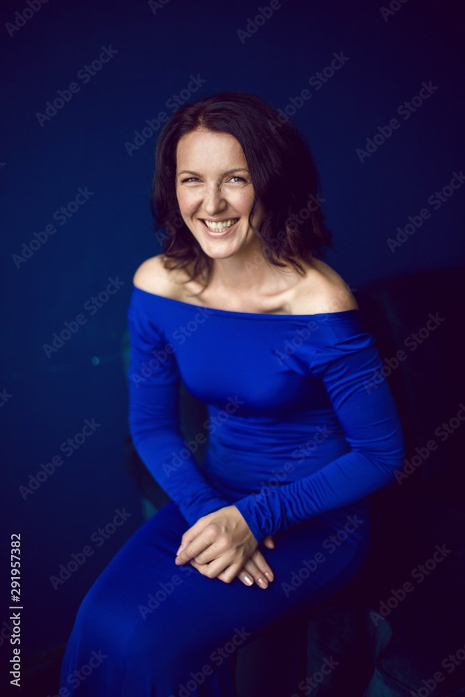 beautiful woman in long blue dress in Studio with blue wall beautiful woman in long blue dress in Studio with blue wall