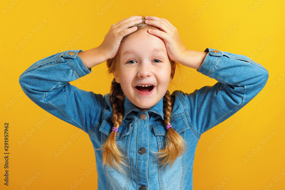 Little girl holds hands behind her head on a yellow background. The ...