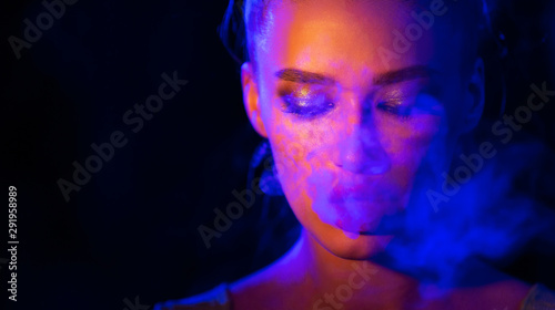 Mysterious girl smoking e-cigarette in neon blue and orange light