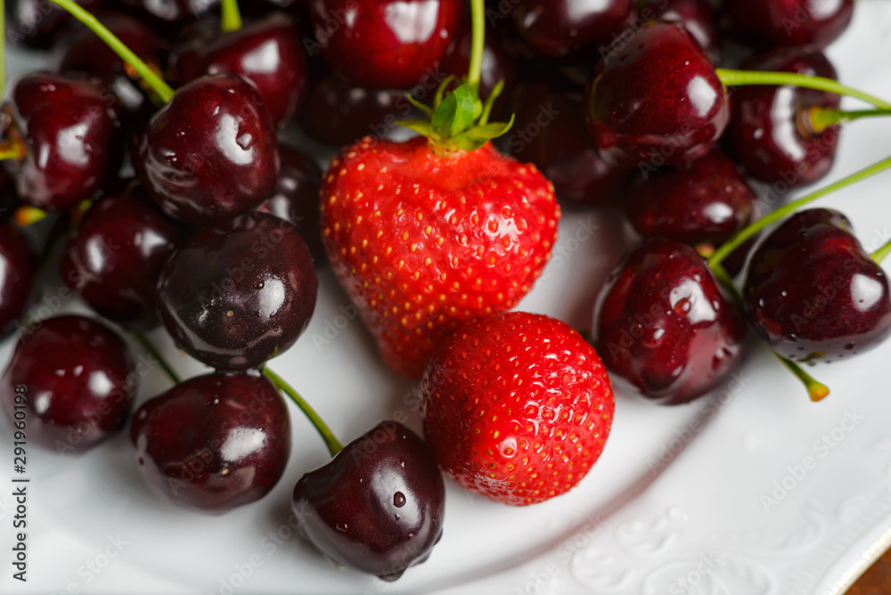 Glossy cherries on a white plate with red strawberries. Ripe and juicy cherry fruits and strawberries Glossy cherries on a white plate with red strawberries. Ripe and juicy cherry fruits and strawberries