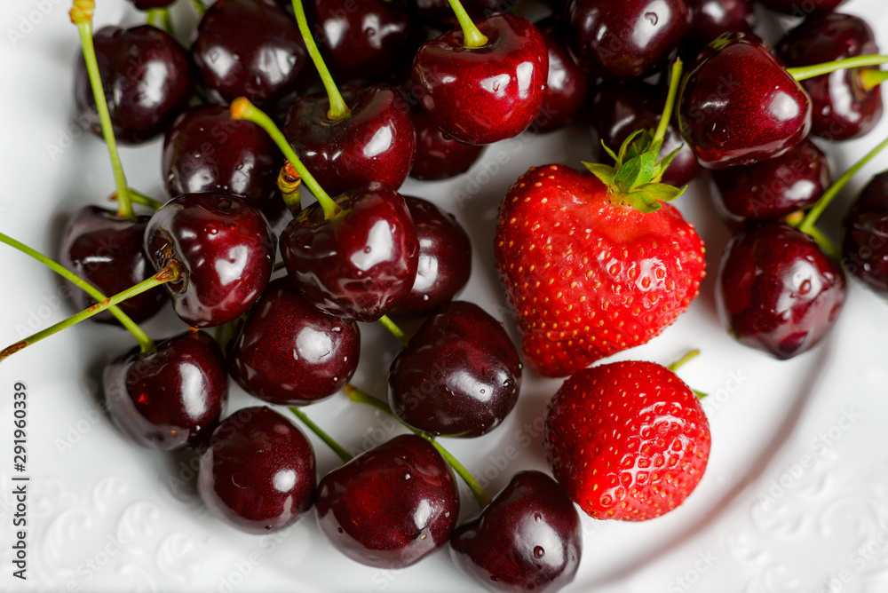 Glossy cherries on a white plate with red strawberries. Ripe and juicy cherry fruits and strawberries Glossy cherries on a white plate with red strawberries. Ripe and juicy cherry fruits and strawberries