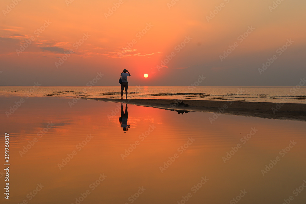 Silhouette of a senior man with a camera taking photo of a beautiful sunset over the Baltic sea in Jurmala, Latvia. Summer evening.