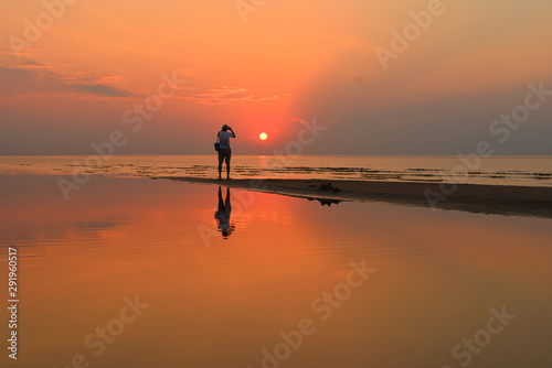 Silhouette of a senior man with a camera taking photo of a beautiful sunset over the Baltic sea in Jurmala, Latvia. Summer evening.
