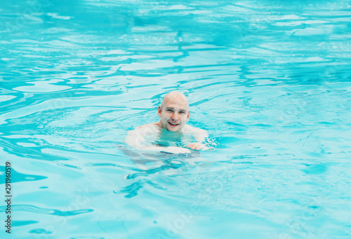 Handsome bald man relaxing resting in swimming pool and smiling