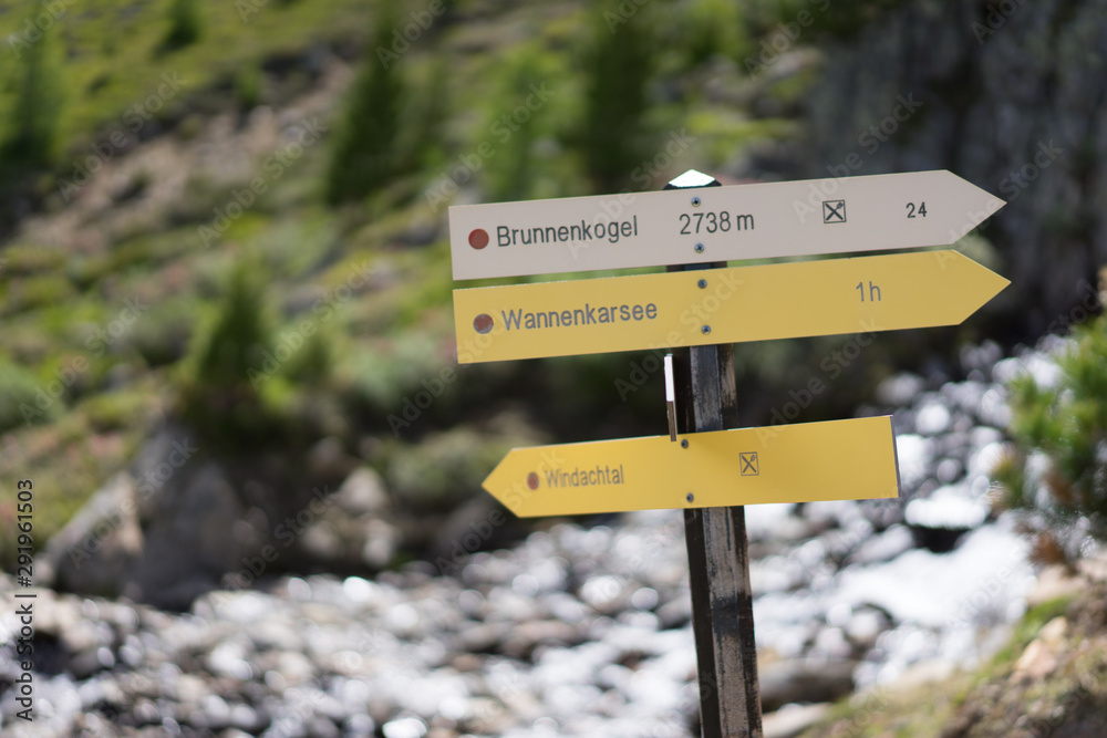 A sign is showing the way in a valley between many mountains.