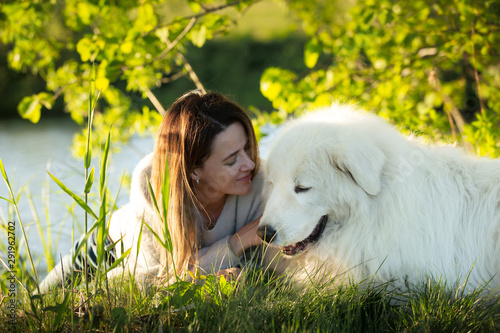 A lovely girl and Cute maremma sheepdog. Big white happy dog breed maremmano abruzzese lying in the forest in summer