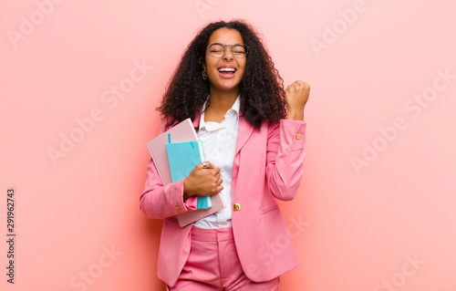 young black pretty business woman with books against pink wall background