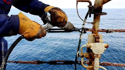 professional seaman in yellow gloves cleans oil tanker metal handrails from rust with special rotating tool close view
