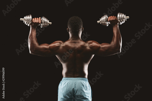 Rear view of black fitness model pushing up the dumbbells