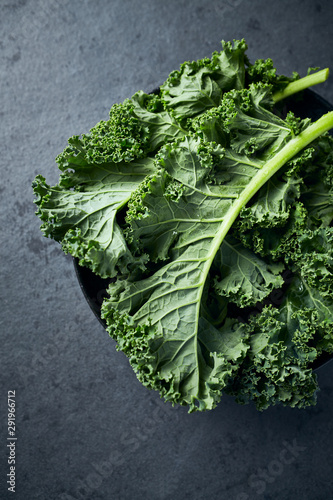 Fresh green kale leaves in a bowl on dark stone background. Healthy food ingredients photo