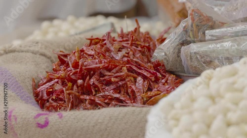 A daylight closeup shot of different types of beans and seeds on display on round trays and plastic weaved sacks in a street food stall along with the other dried ingredients.. photo