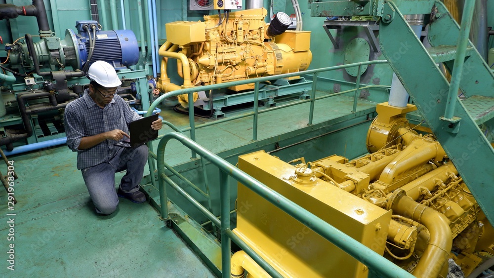 Asian engineer working in engine room. He using laptop in engine