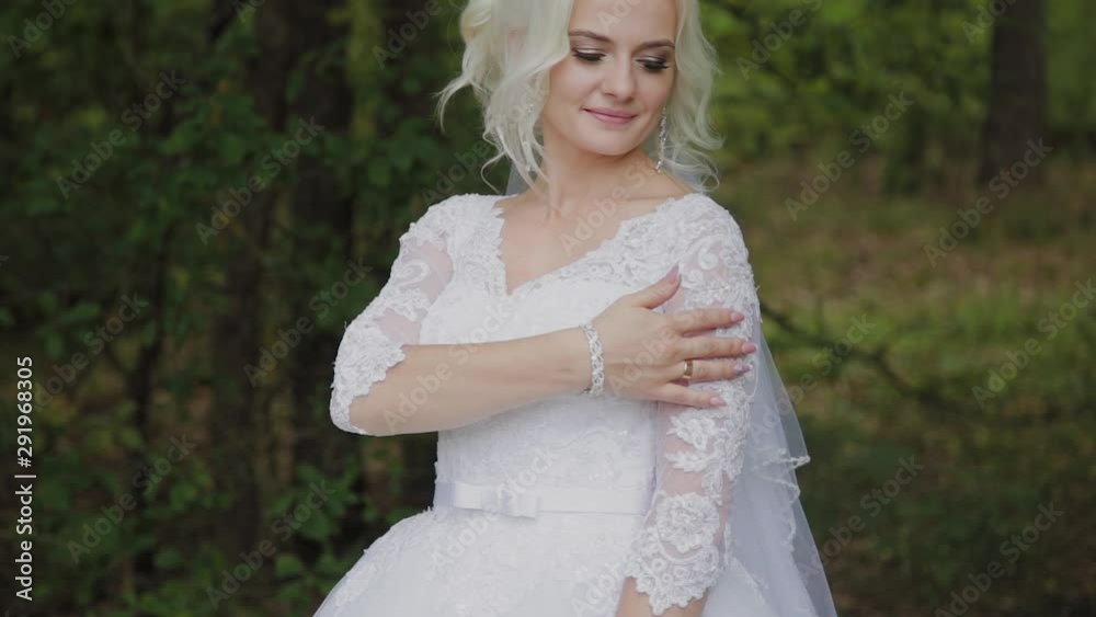 Beautiful blonde bride in the forest strokes herself, straightens her hair.