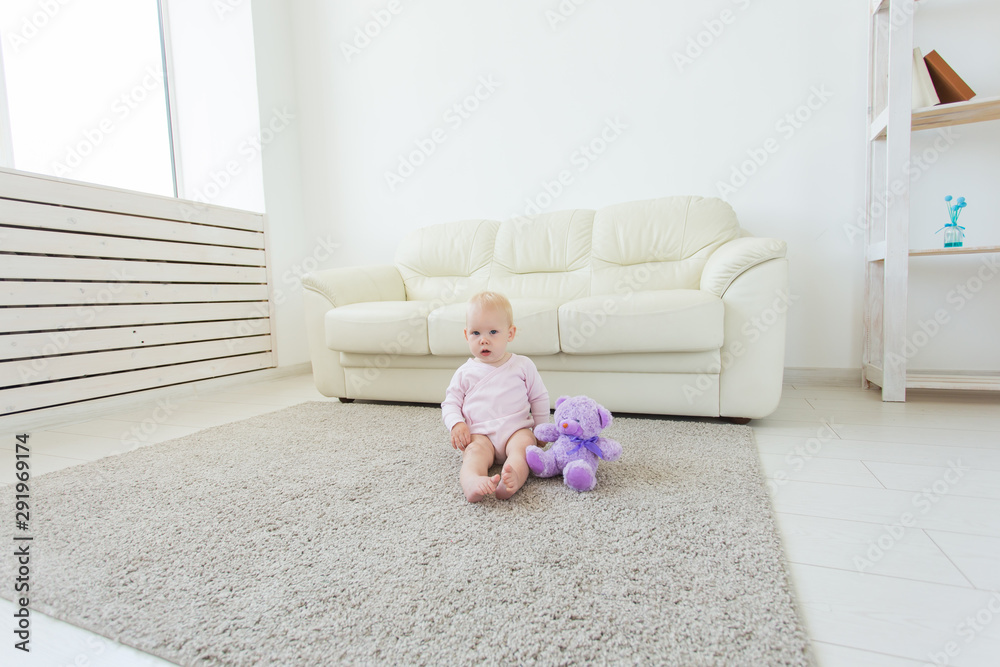 Childhood, children and babyhood concept - Adorable blonde baby sitting on the floor Childhood, children and babyhood concept - Adorable blonde baby sitting on the floor