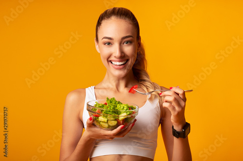 Leinwand Poster Fitness Girl Eating Vegetable Salad Standing Over Yellow Background