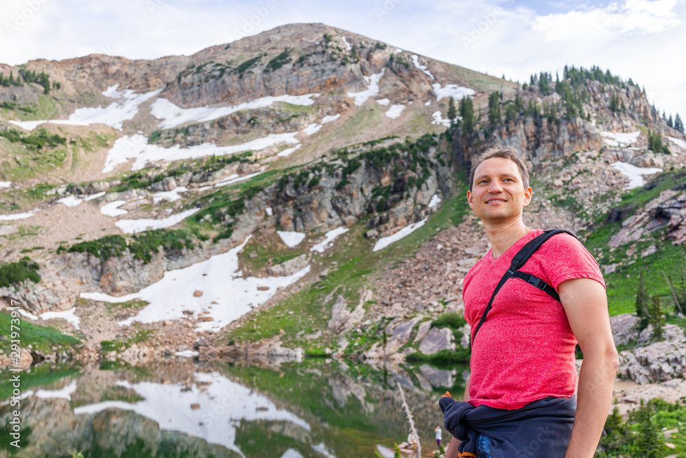 Albion Basin, Utah summer with happy man standing by reflection of water on Cecret Lake in Wasatch mountains with rocks, snow and green color