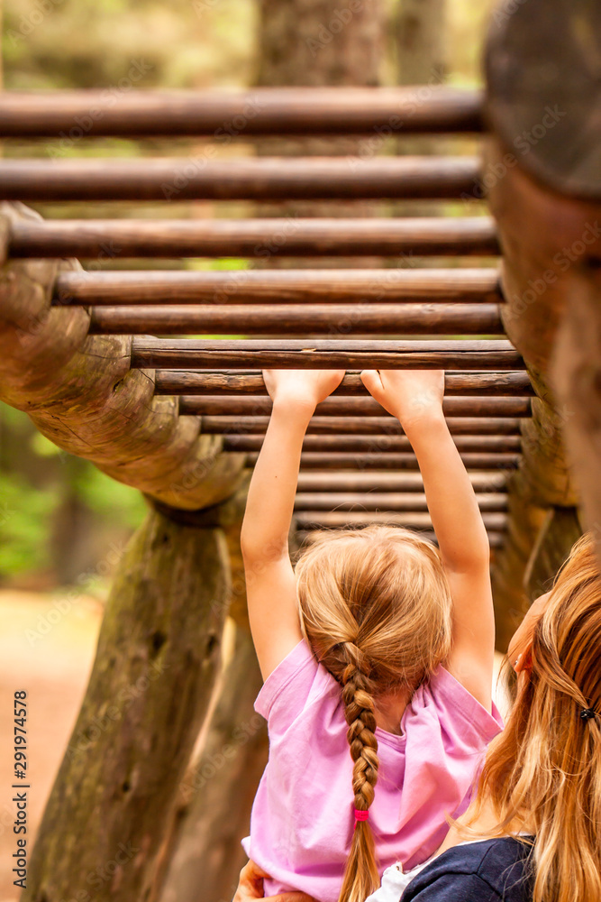 Mother Supporting daughter in the playground with climbing and hanging on a ladder Mother Supporting daughter in the playground with climbing and hanging on a ladder