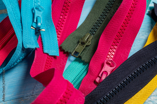Pack lot of colorful plastic and metal zippers stripes with sliders pattern for handmade sewing tailoring on the blue painted wooden background close up selective focus