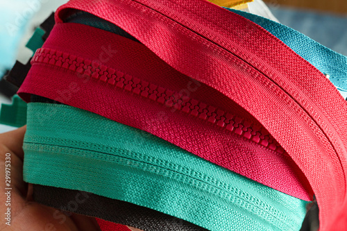 Pack lot of colorful plastic and metal zippers stripes with sliders pattern for handmade sewing tailoring on the blue painted wooden background close up selective focus