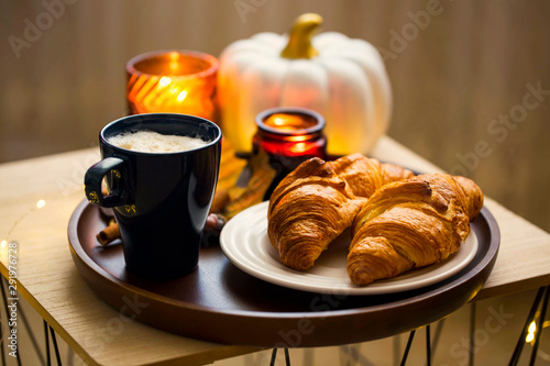 Cozy autumn morning breakfast with coffee cup, croissants and candles, cozy home