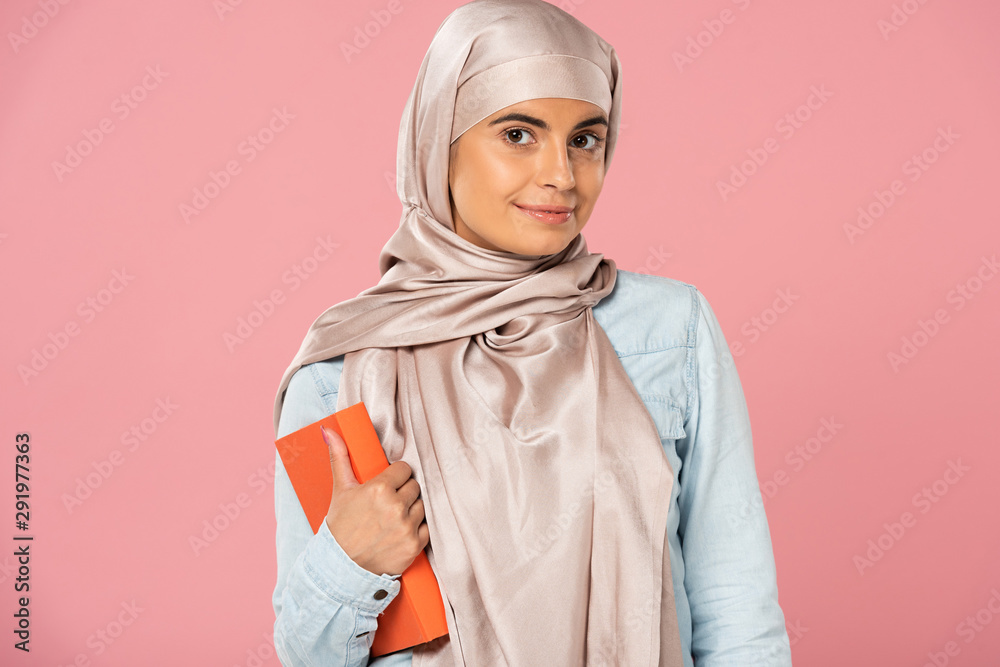 Fototapeta premium attractive muslim student in hijab holding book isolated on pink